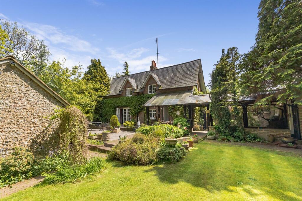 The ivy-covered front of Grange Farm Cottage with its garden lawn on a sunny day