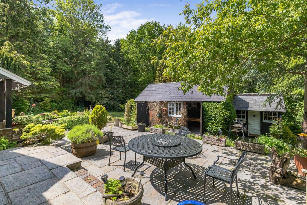 The sunny garden patio with seating beneath mature trees
